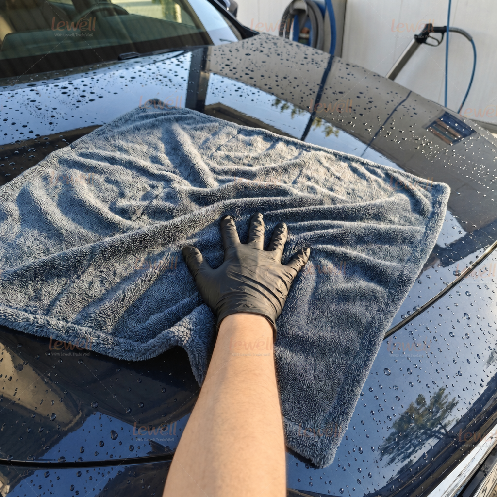 Gray twisted-loop car drying towel laid on car hood, hand smoothing fabric