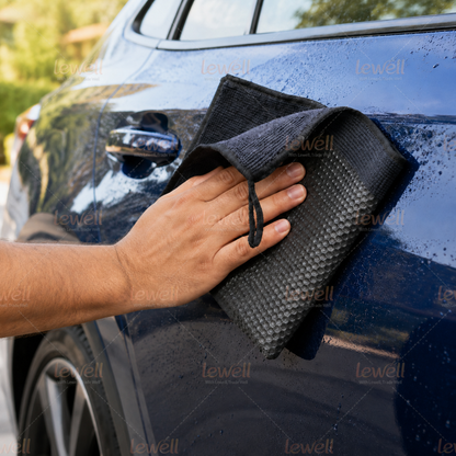 Black clay decontamination towel being used on car paint, held in hand